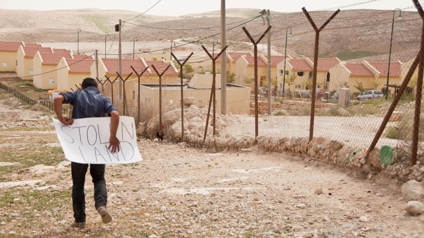Homme près d'une frontière avec un panneau indiquant "terre volée"