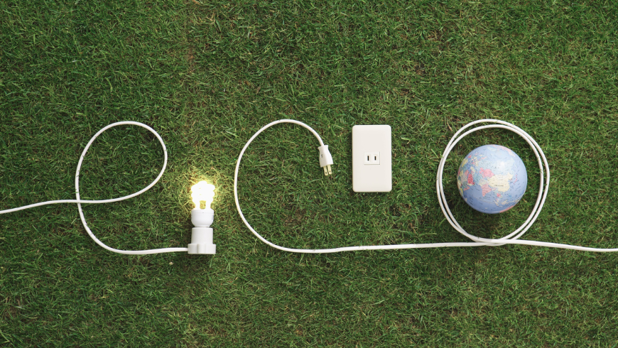 Ampoule et prises électriques sur une pelouse verte formant le mot « éco » avec la planète Terre, symbolisant l'énergie durable et la conscience environnementale.