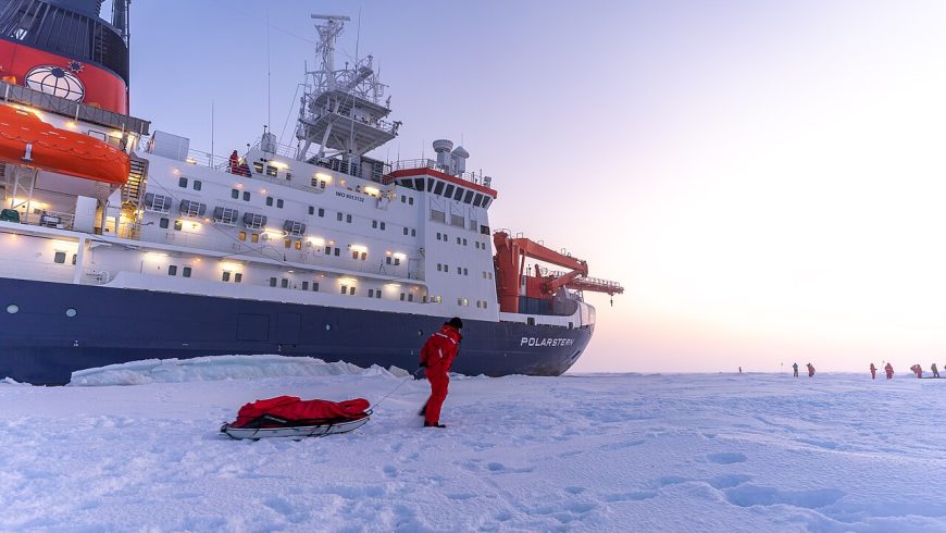 Scientifique debout sur la glace de mer arctique devant le navire de recherche RV Polarstern lors d'une expédition scientifique