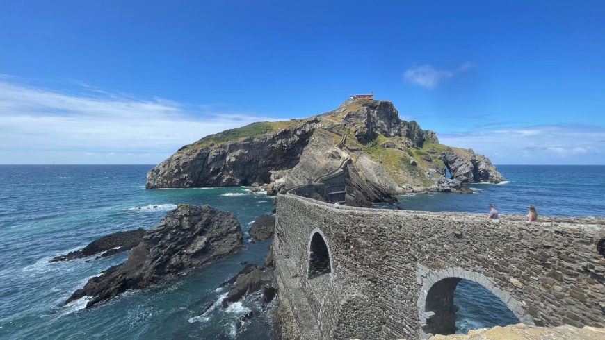 l'Ermitage de San Juan de Gaztelugatxe avec le pont de pierre au premier plan et deux personnes qui le traversent