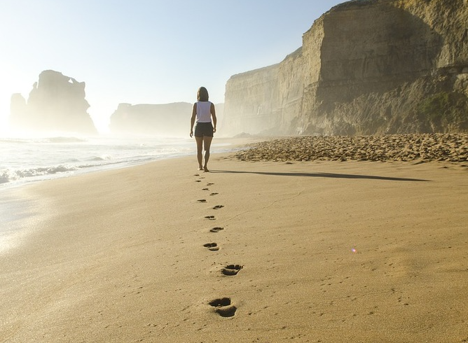 Femme marchant pieds nus sur une plage, laissant des empreintes dans le sable